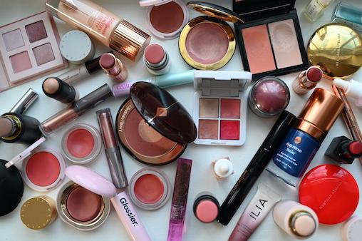 A variety of cosmetics and beauty products, some open, some new, spread out on a table.